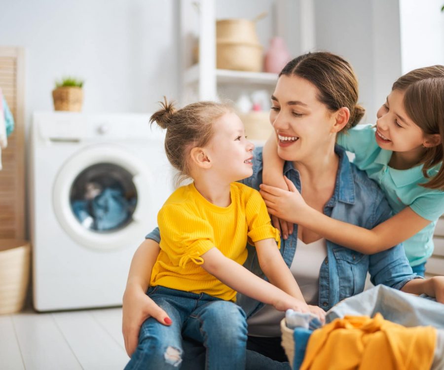 Beautiful young woman and child girl little helper are having fun and smiling while doing laundry at home.