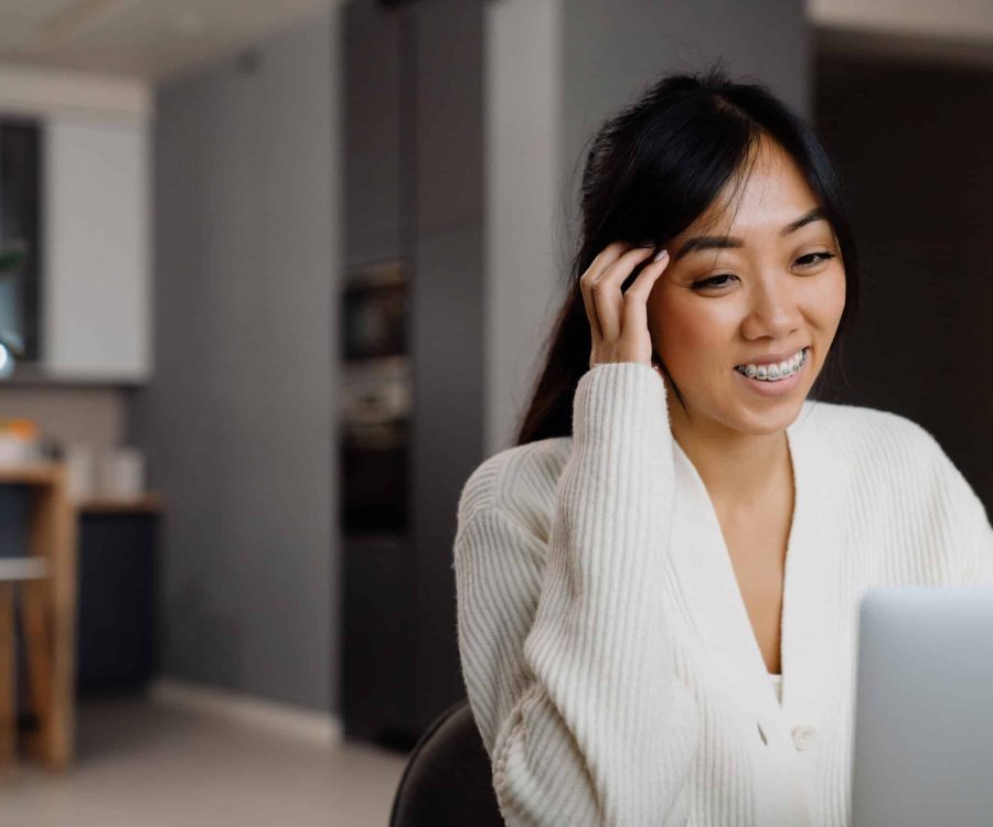Asian woman with brace laughing while working with laptop at home